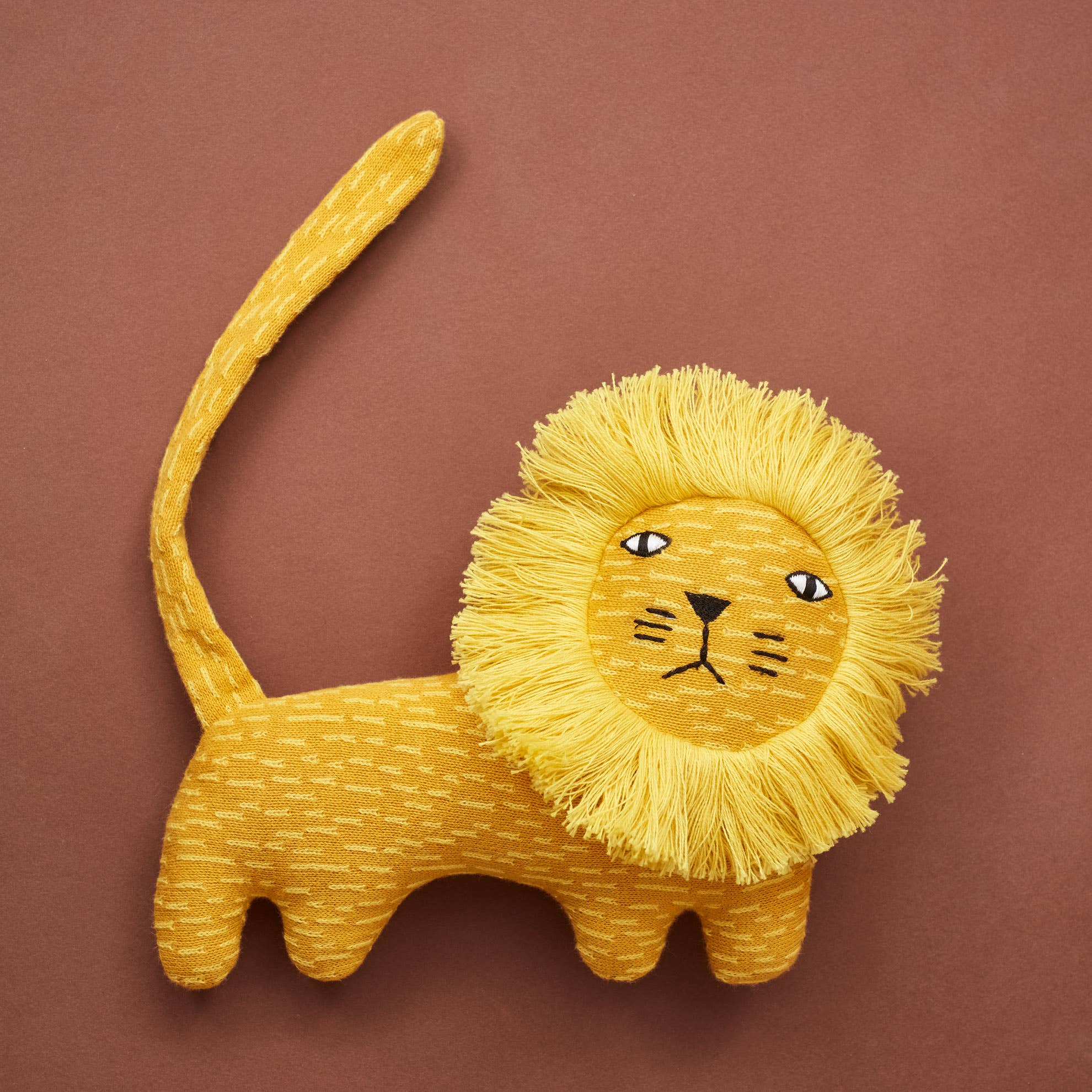A yellow knit lion creature with a fluffy mane, tail, and details, set against a brown background.