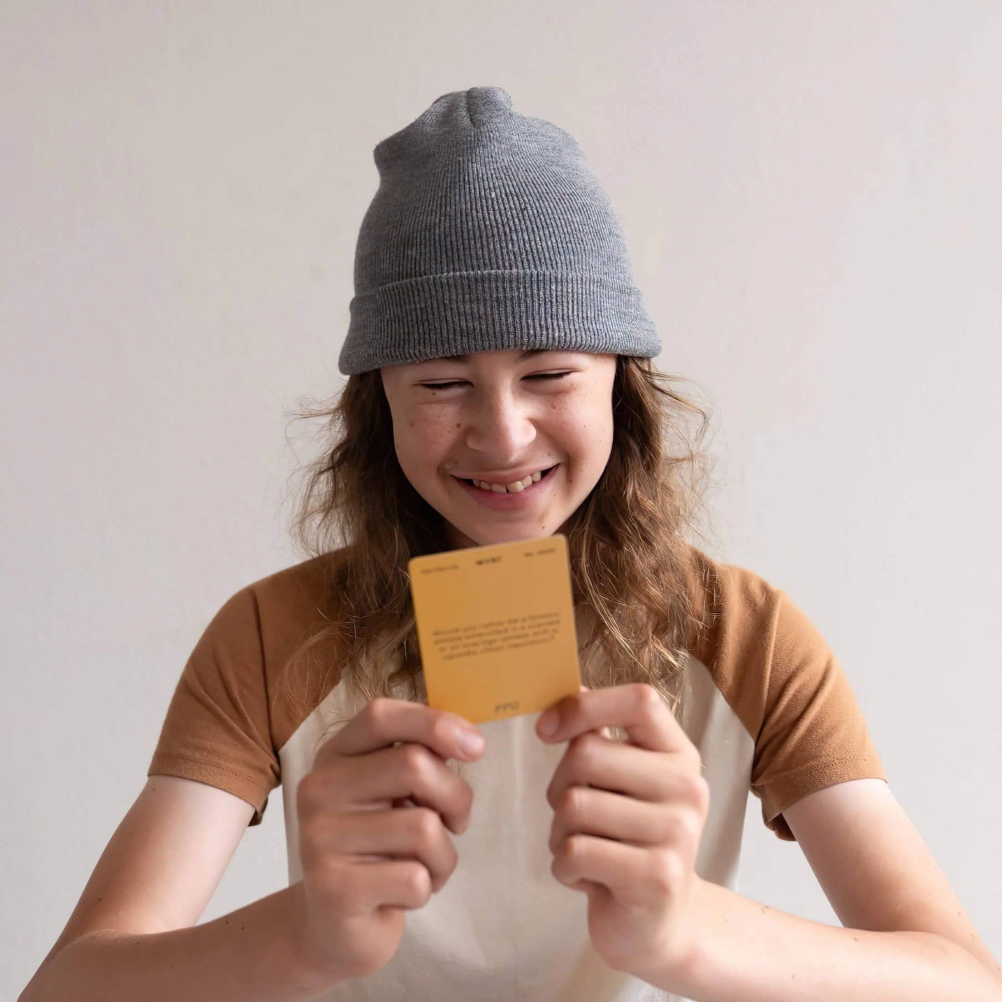 Child wearing a gray beanie holding a yellow card against a plain background