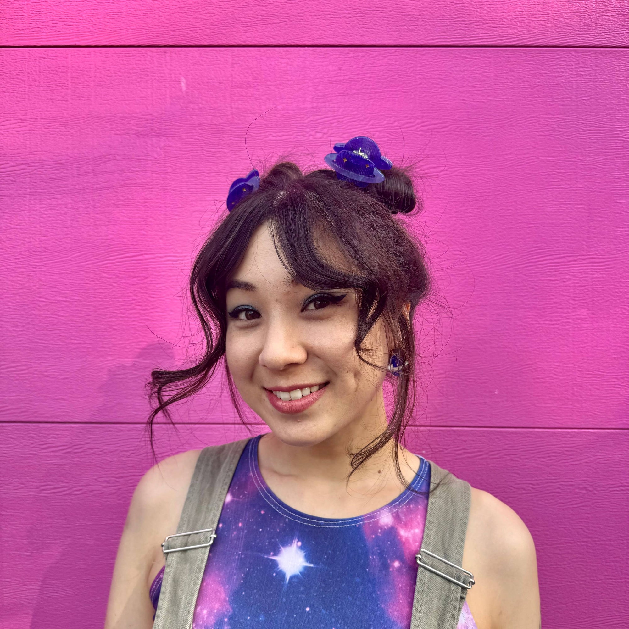 Person wearing a galaxy-themed tank top and overalls against a pink background