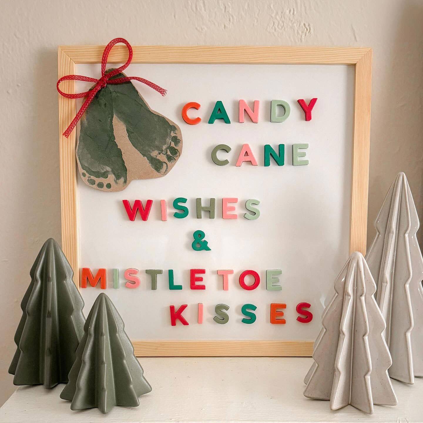 Decorative sign with Christmas-themed text and candy cane design, surrounded by small trees on a neutral background.