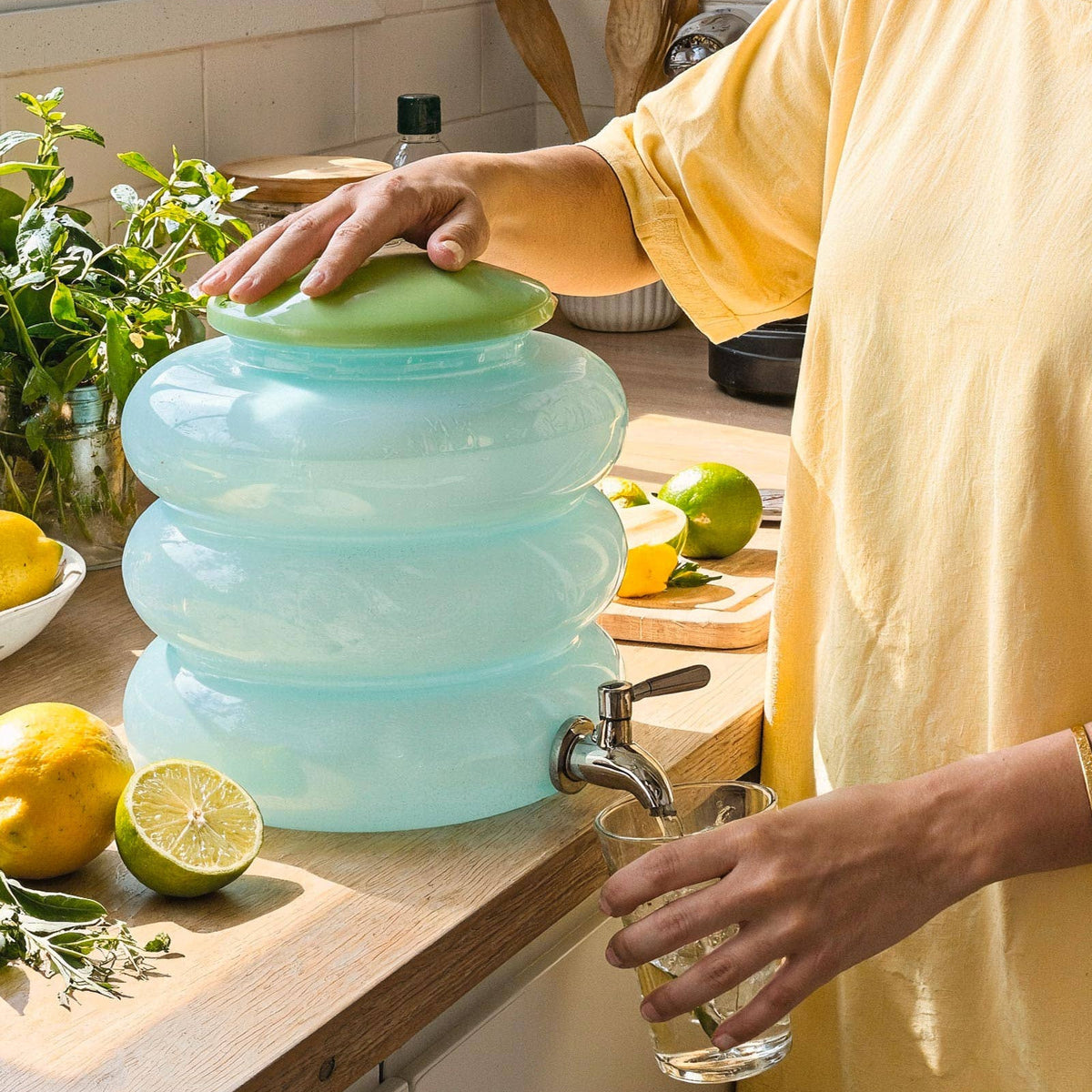 Person using a glass water container with a faucet in a kitchen.