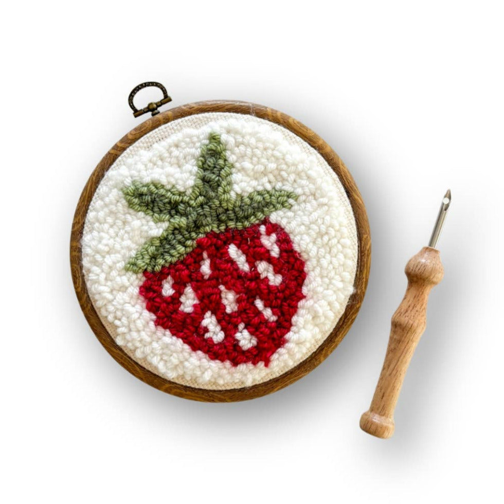Embroidery hoop with a strawberry design and a crochet hook on a white background