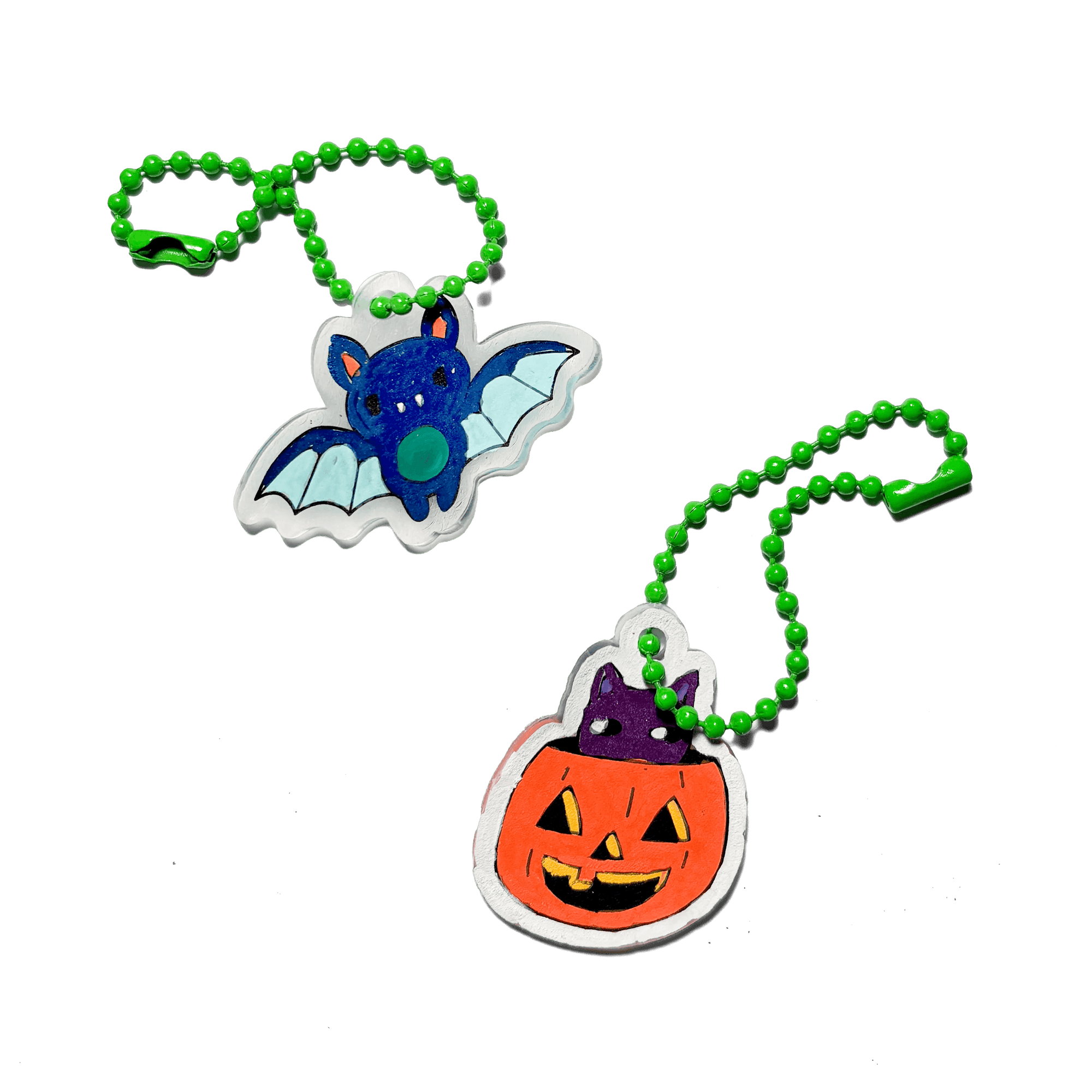 Two Halloween-themed keychains, one shaped like a bat and the other like a pumpkin, on a green background.