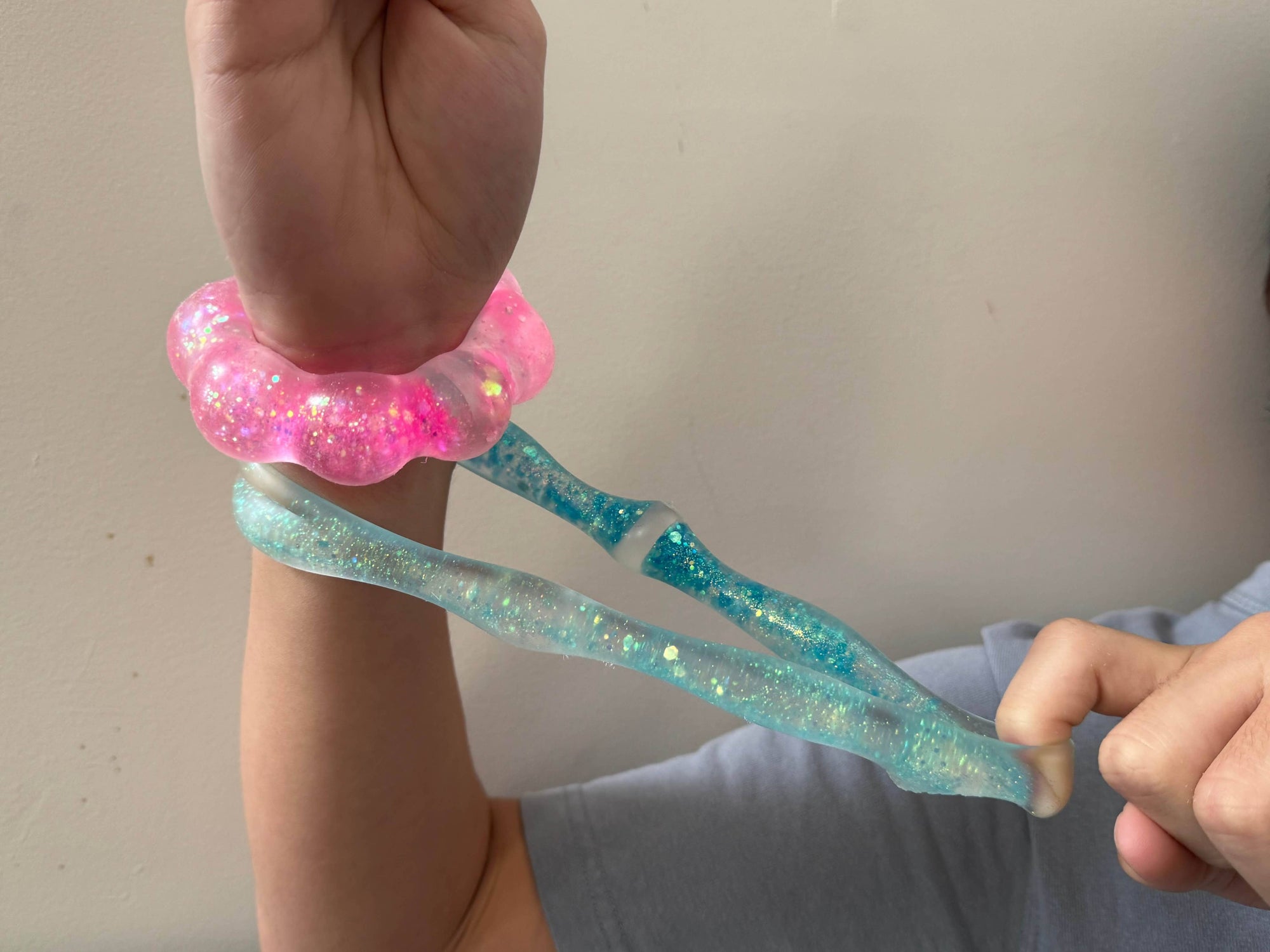 Person wearing a pink glittery bracelet on a light gray background
