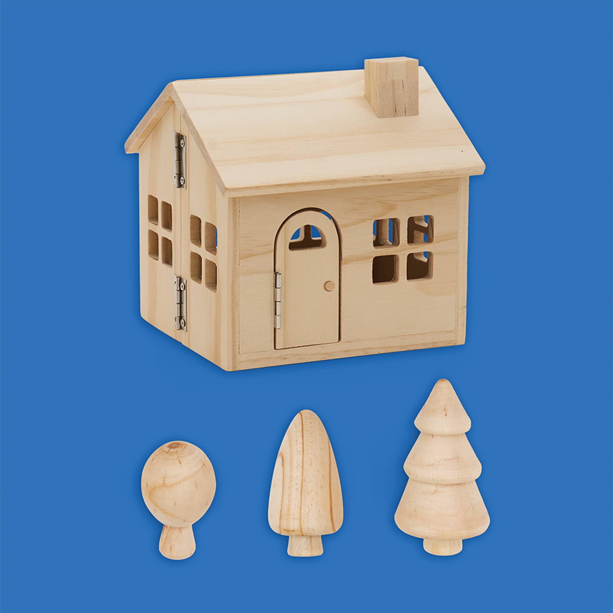 A small unfinished wooden house toy or model with a pitched roof, arched door, windows, and a chimney, shown on a solid blue background with three loose wooden decorative pieces below it.
