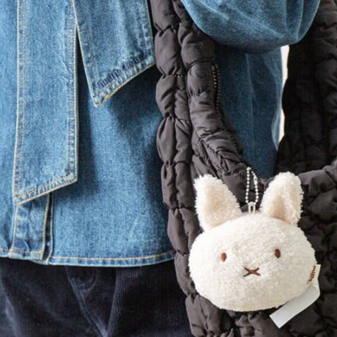 Person wearing a denim jacket with a black quilted bag featuring a plush bunny character.