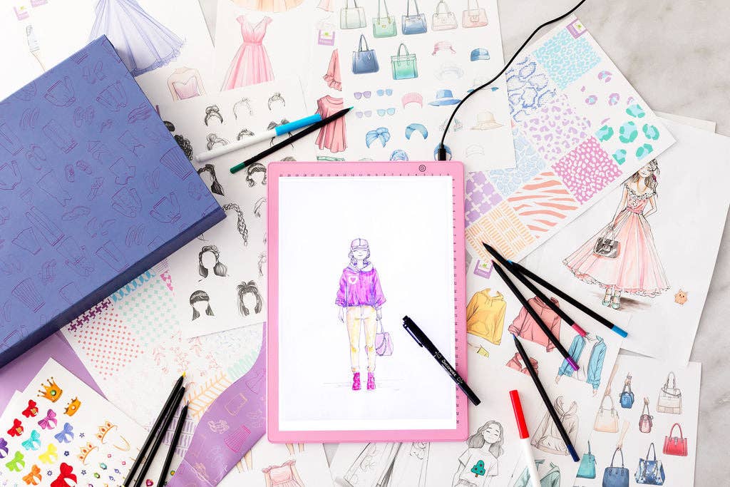 Artistic illustrations of fashion and accessories on a surface with drawing tools.