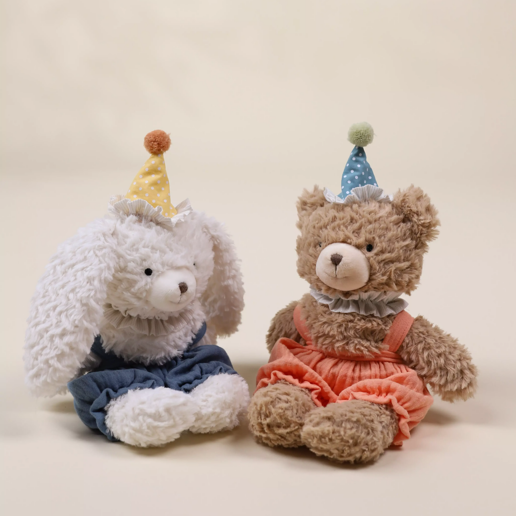 Two stuffed animals, a gray elephant and a brown bear, wearing party hats on a plain background.