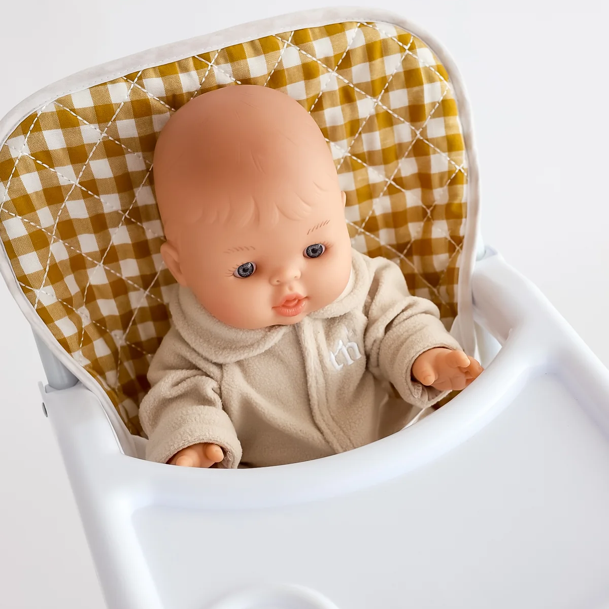 Baby doll in a high chair with a checkered cushion on a white background