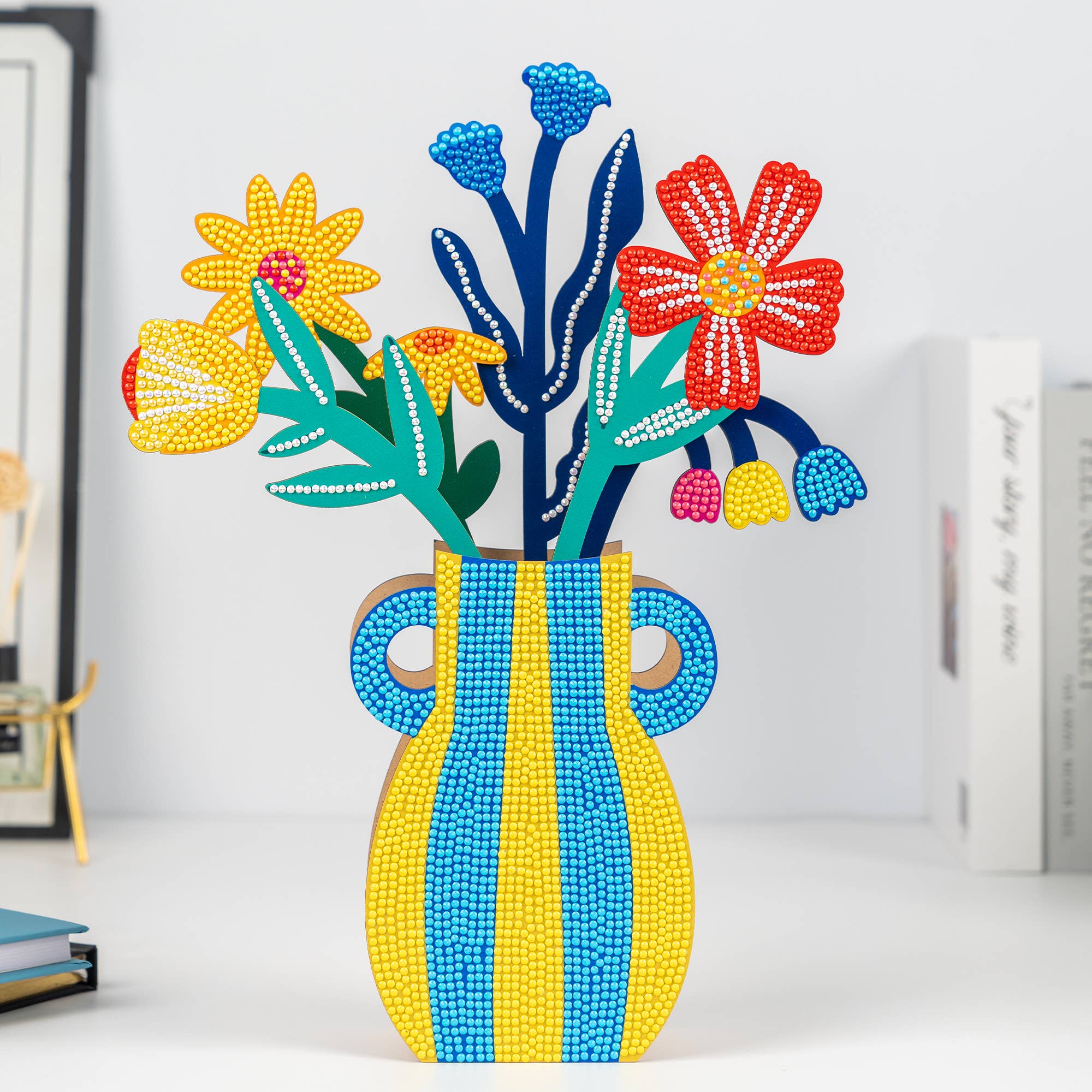 Colorful beaded flower arrangement in a striped vase on a white surface.