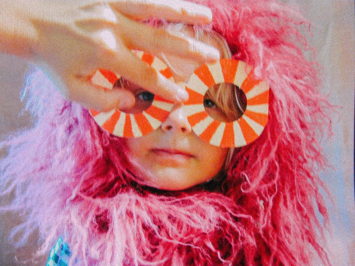 Person wearing a pink feathered headpiece and orange and white circular sunglasses.