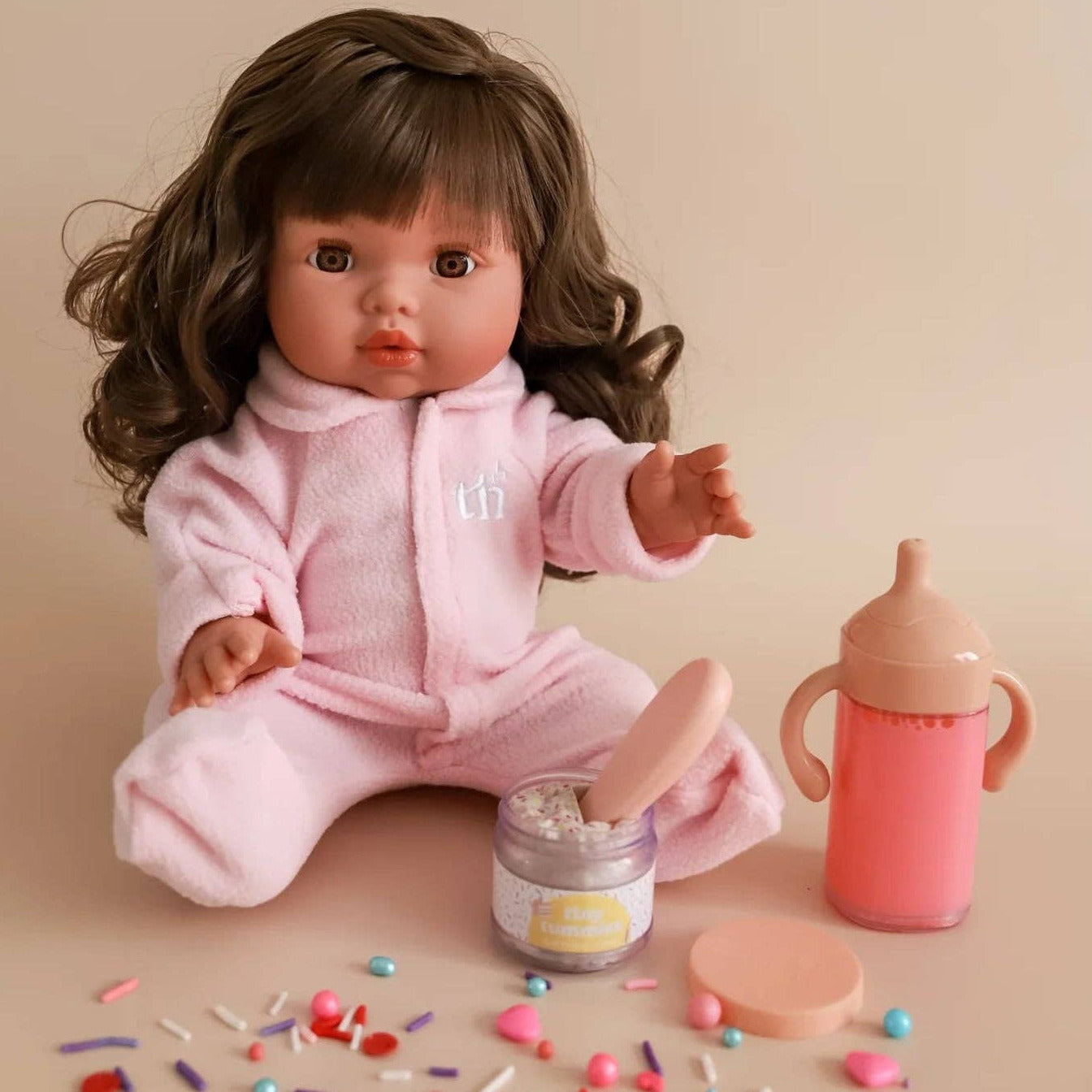 Doll in pink outfit with a bottle and toys on a beige background