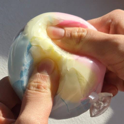 Hand holding a colorful squishy toy with a heart-shaped object inside.