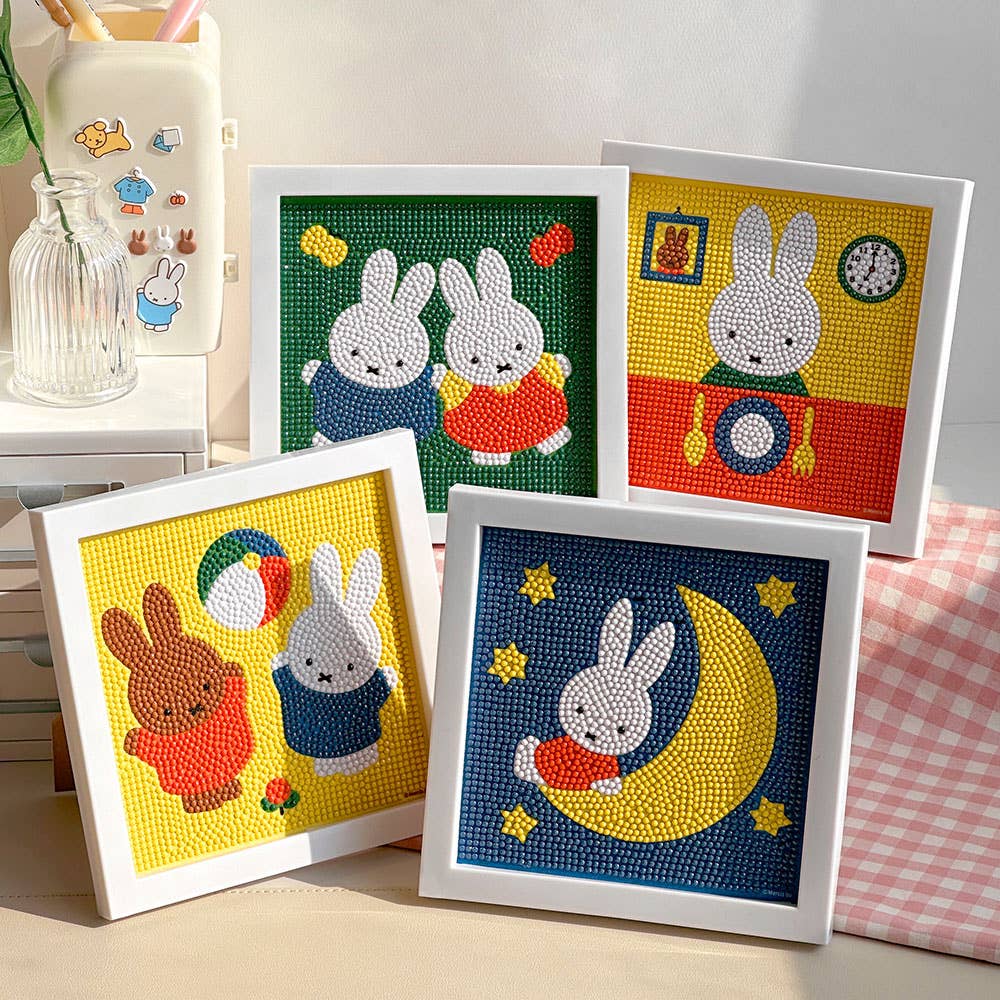Four framed diamond painting artworks of bunnies on a table with a checkered cloth.