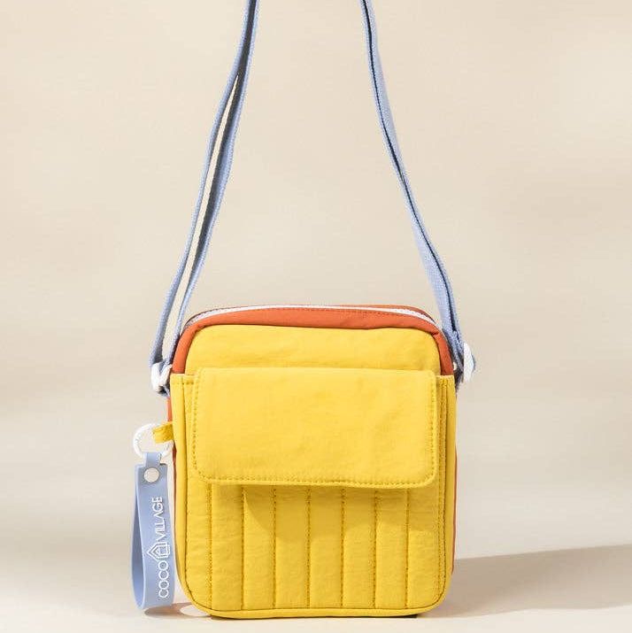 Yellow crossbody bag with a blue strap on a beige background