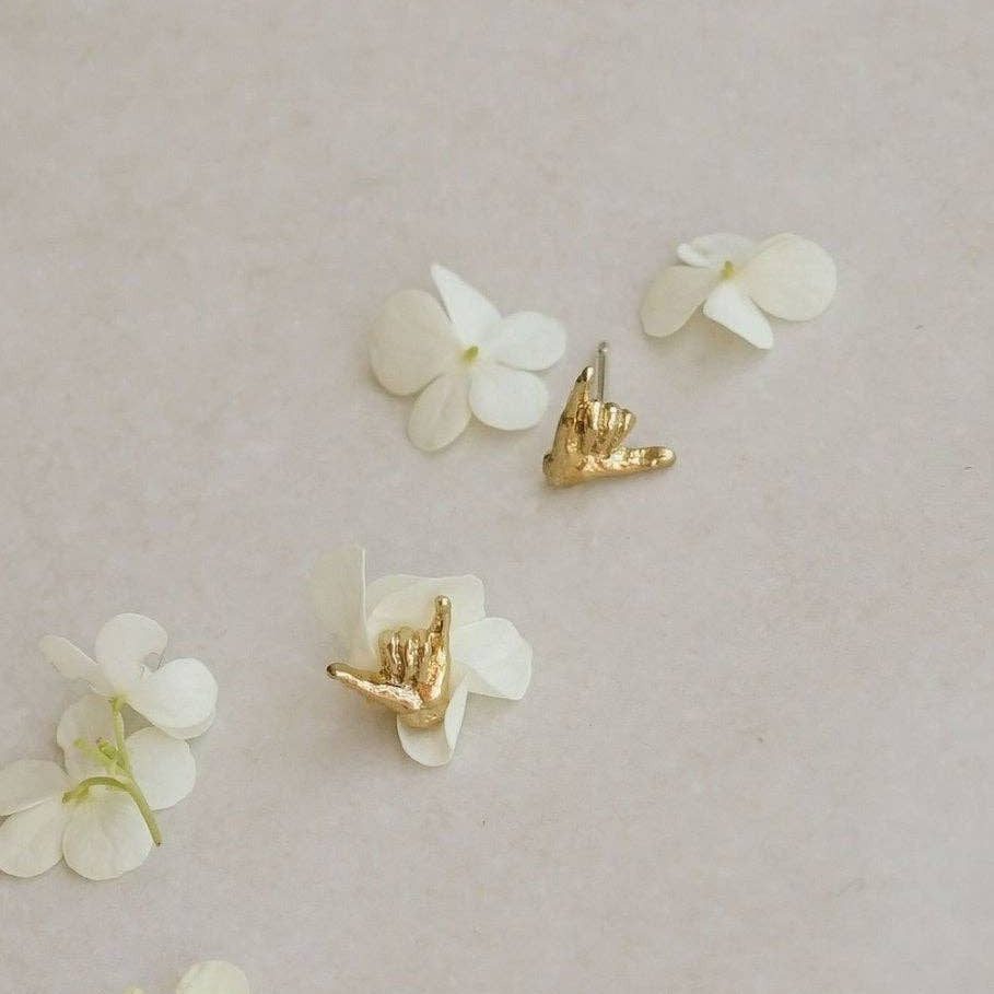 Gold hand gesture earrings on white flowers against a beige background