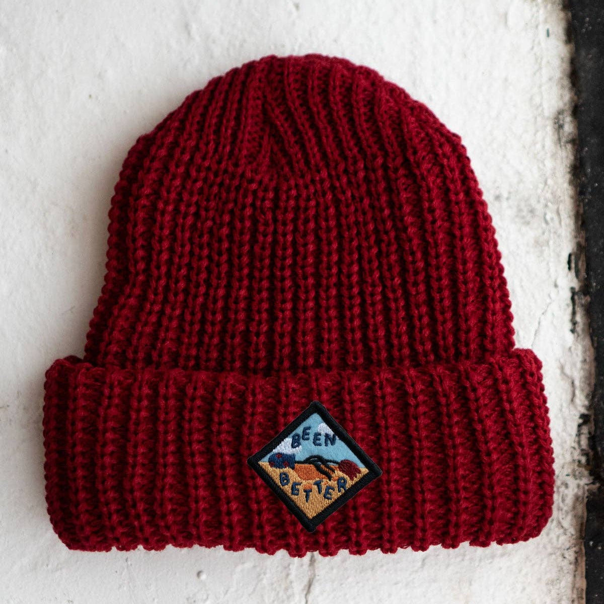 Red knit beanie with a logo on a white textured background