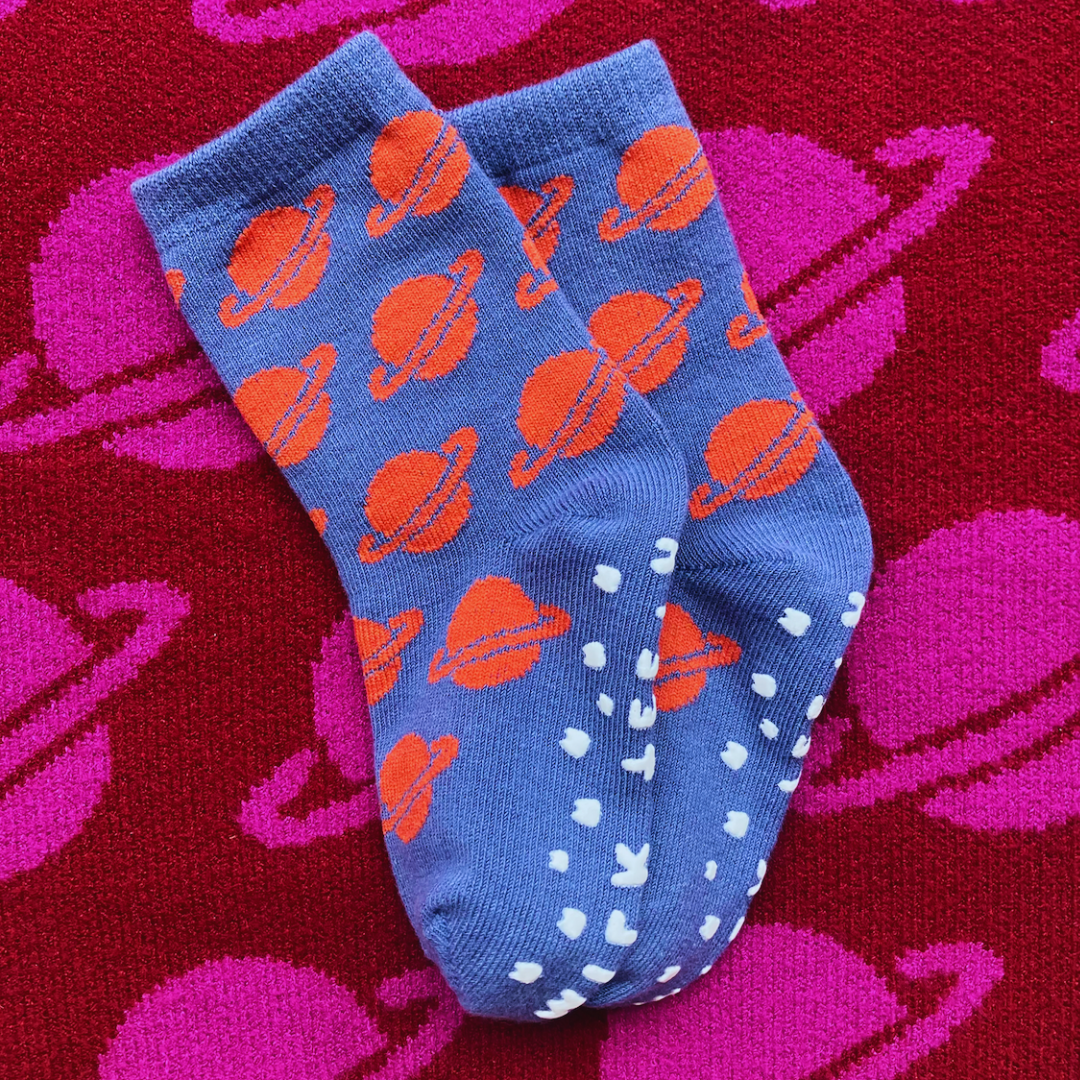 Blue socks with orange planet patterns on a red background with pink Saturn shapes.