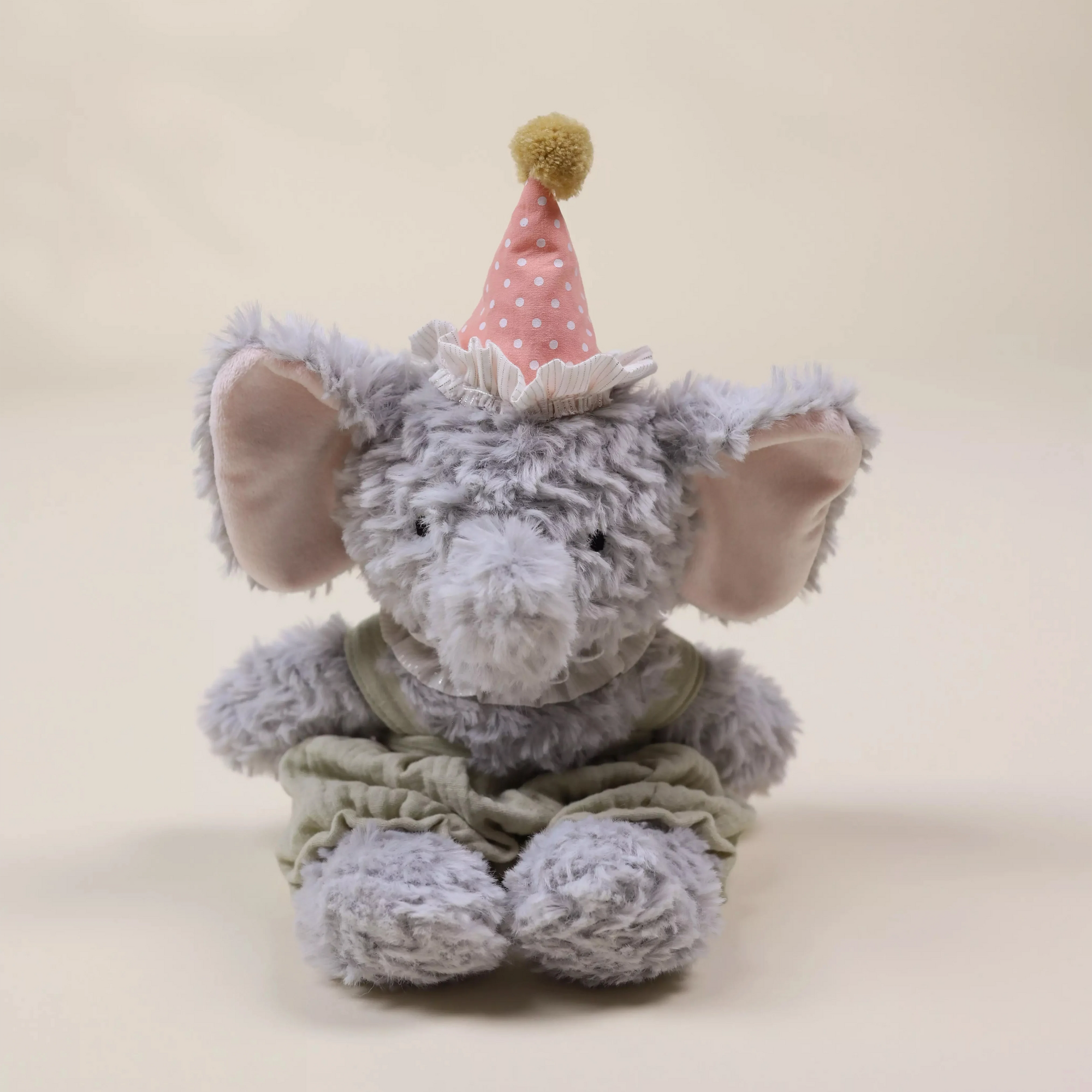 Plush elephant toy with a party hat on a beige background