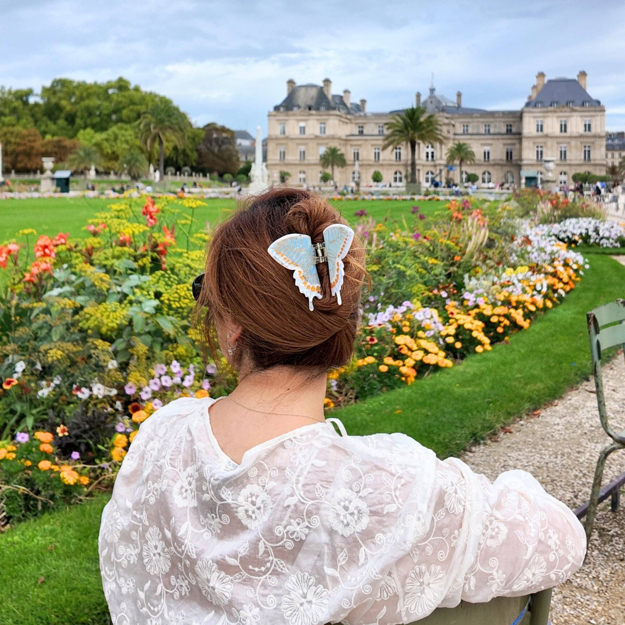 Woman sitting in a garden with flowers and a building in the background