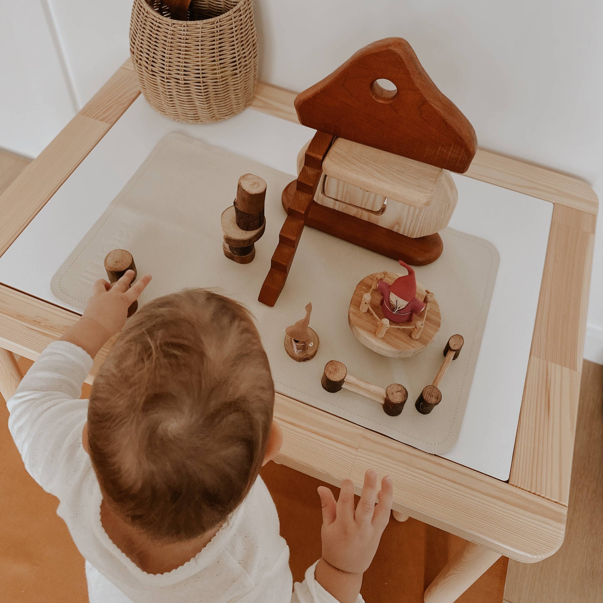 Child playing with wooden toys on a table in a minimalistic room.