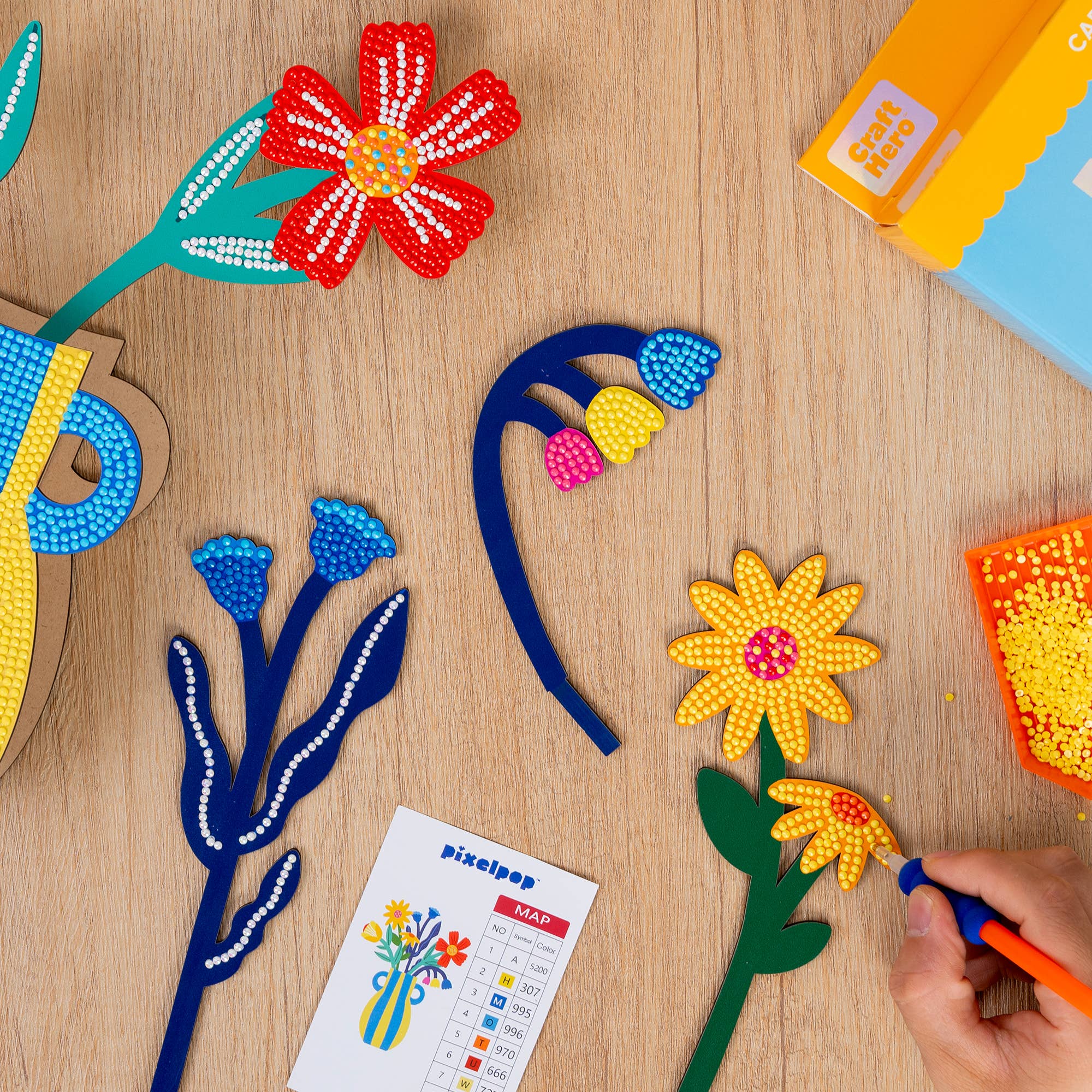 Colorful flower designs being created with beads on a wooden surface, featuring a 'pixelpop' kit.