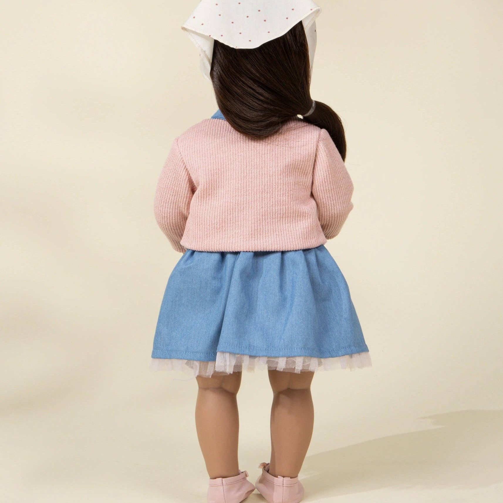 doll wearing a pink sweater and blue skirt with a white hat on a beige background