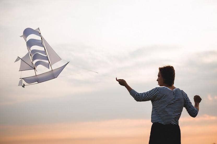 Person flying a sailboat-shaped kite against a sunset sky