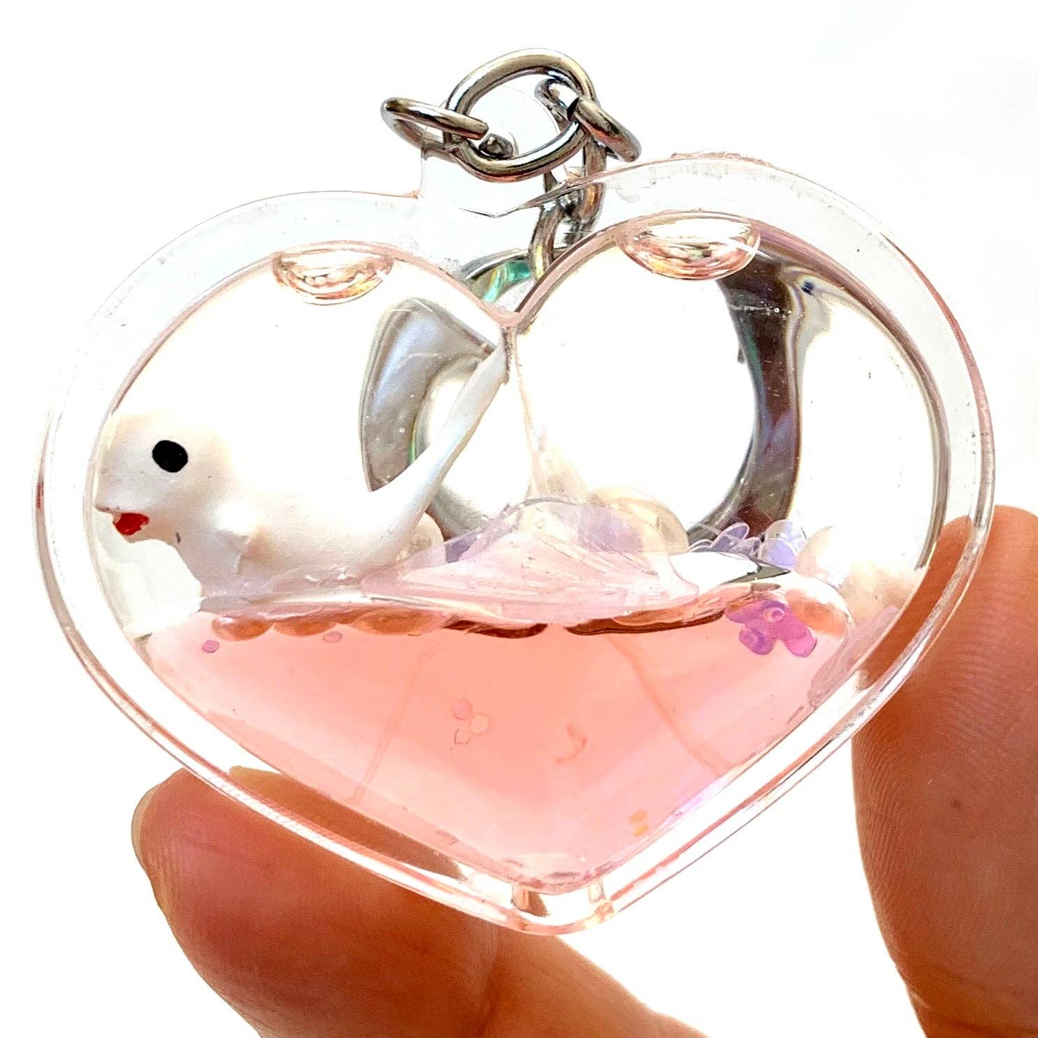 Heart-shaped keychain with a small white animal figure inside, held by a hand.