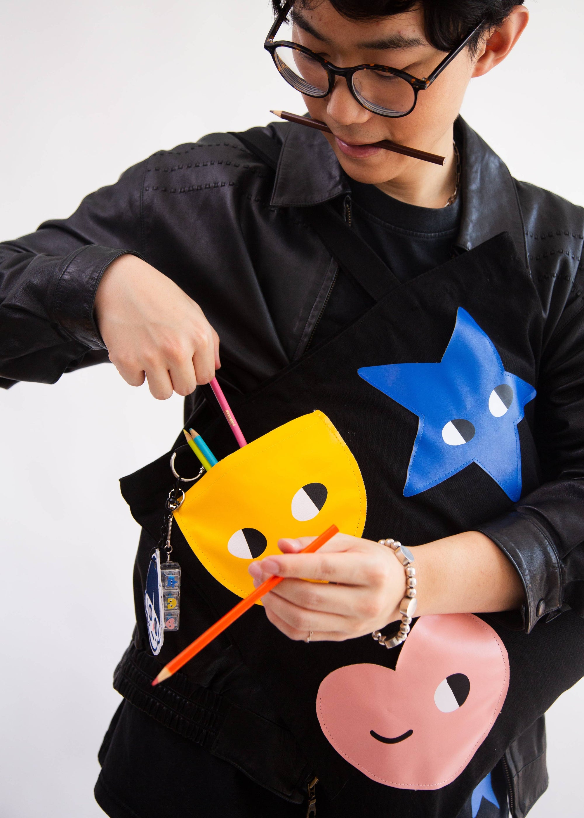 Person wearing a black jacket with colorful face designs, holding a pen.