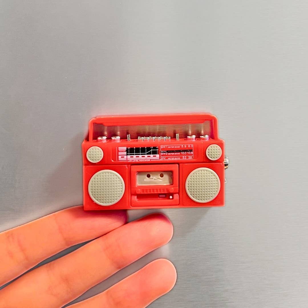 Red miniature radio with cassette player held between fingers on a gray background