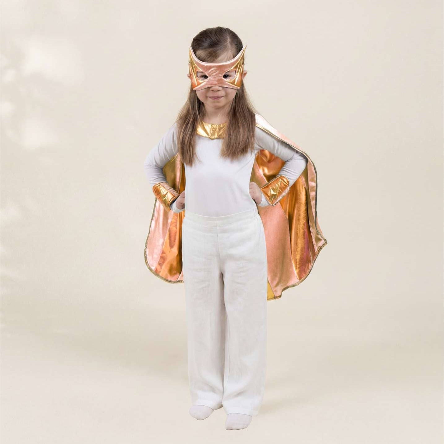 Child wearing a superhero costume with a gold cape and mask on a plain background