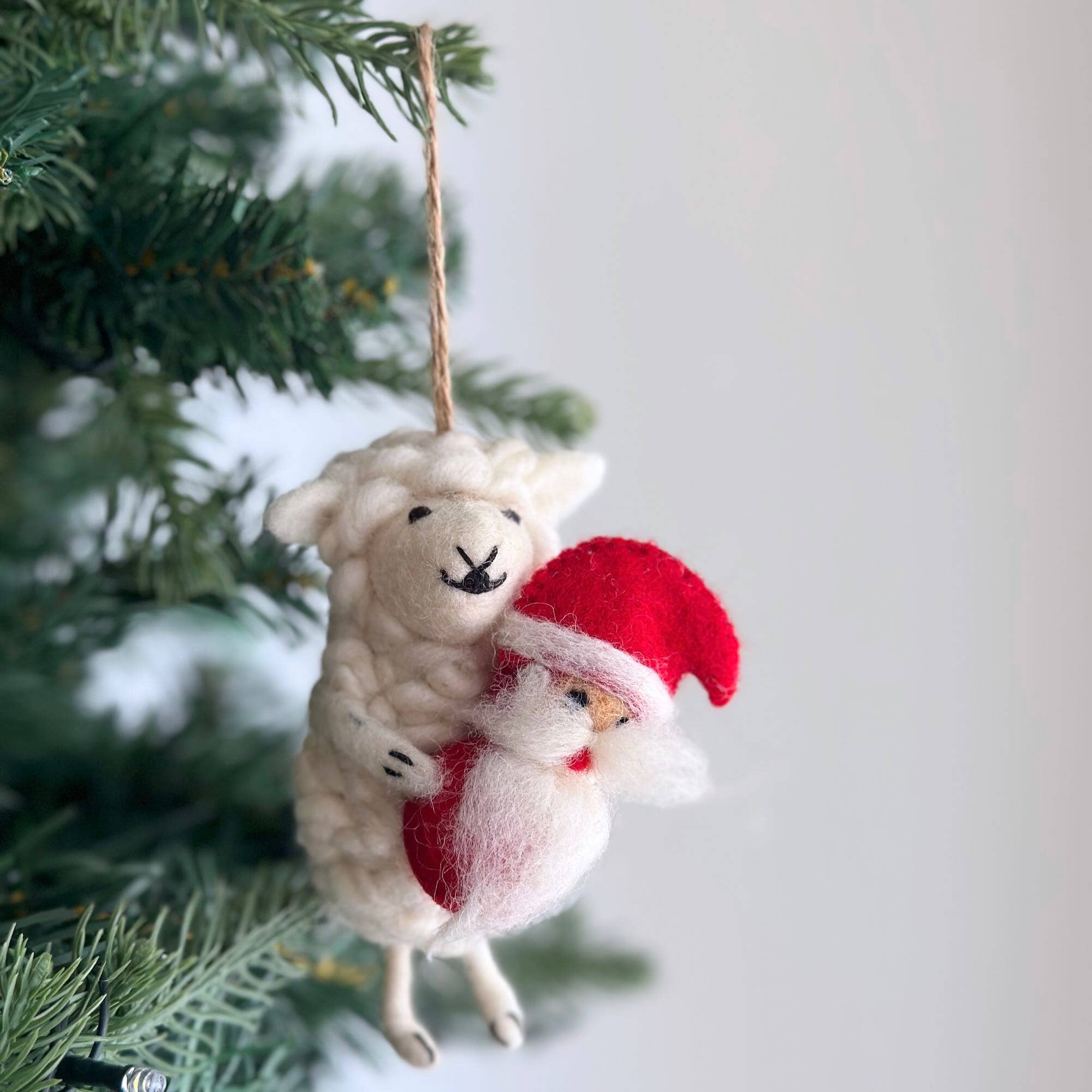 Decorative Christmas ornament with a sheep and Santa Claus figure hanging on a tree.