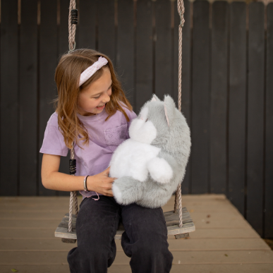 Child on a swing holding a plush toy in a backyard setting