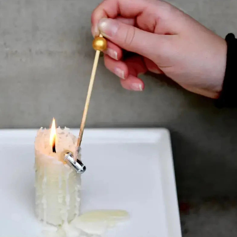 Hand using a wooden pick to retrieve items from a candle on a white plate with a gray background