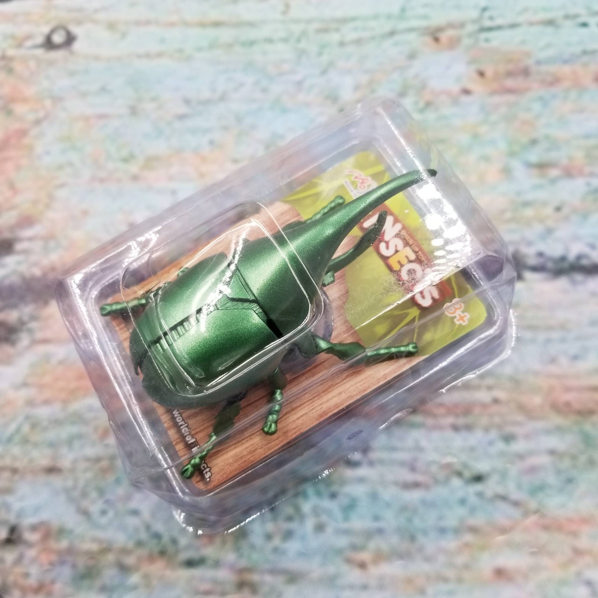 Green toy beetle in packaging on a textured surface