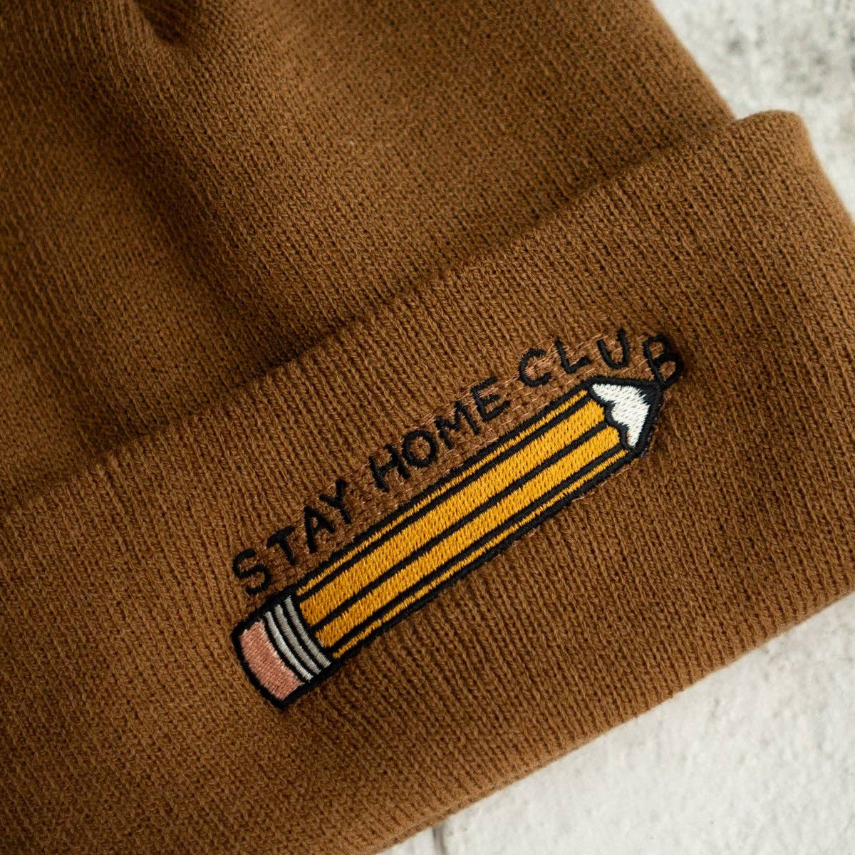 Brown beanie with 'Stay Home Club' pencil patch on a light background