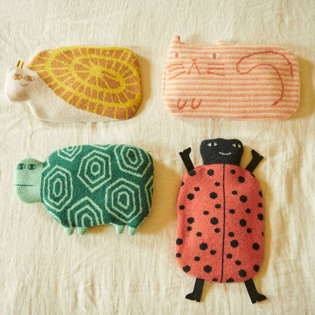 Four whimsical, handcrafted fabric pouches shaped like a turtle, a striped cat, a patterned turtle, and a ladybug, arranged on a textured off-white fabric background.