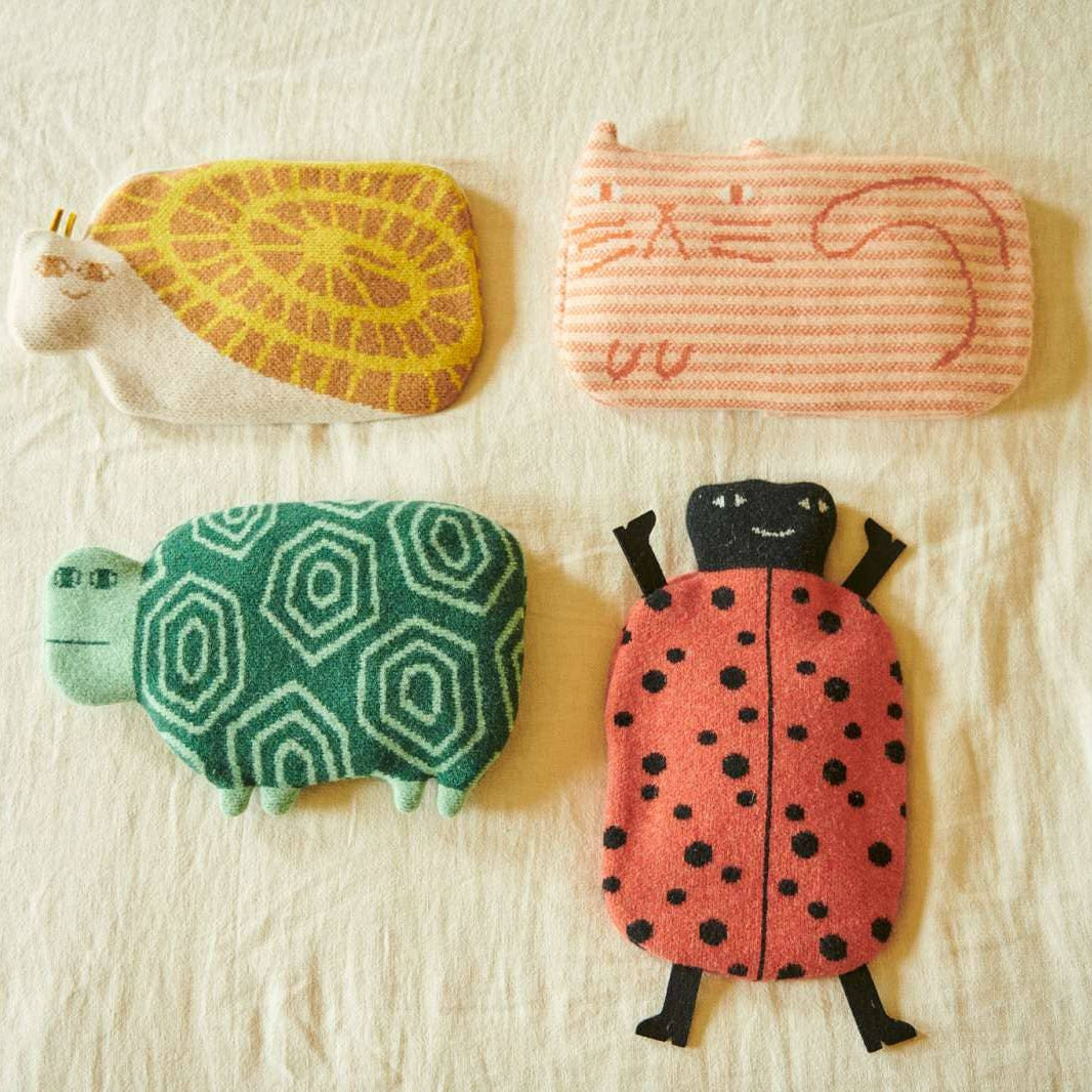 Four whimsical, handcrafted fabric pouches shaped like a turtle, a striped cat, a patterned turtle, and a ladybug, arranged on a textured off-white fabric background.