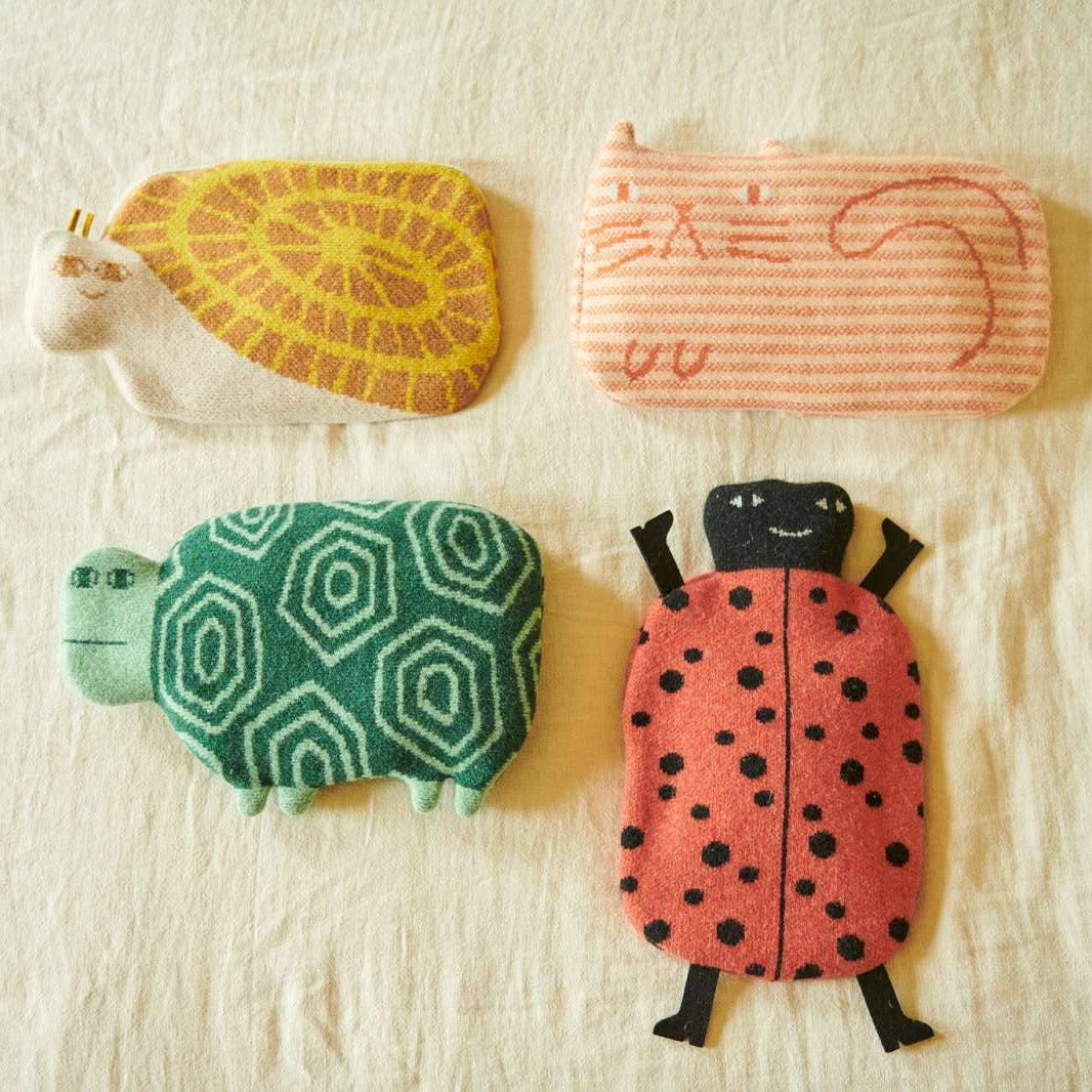 Four whimsical, handcrafted fabric pouches shaped like a turtle, a striped cat, a patterned turtle, and a ladybug, arranged on a textured off-white fabric background.