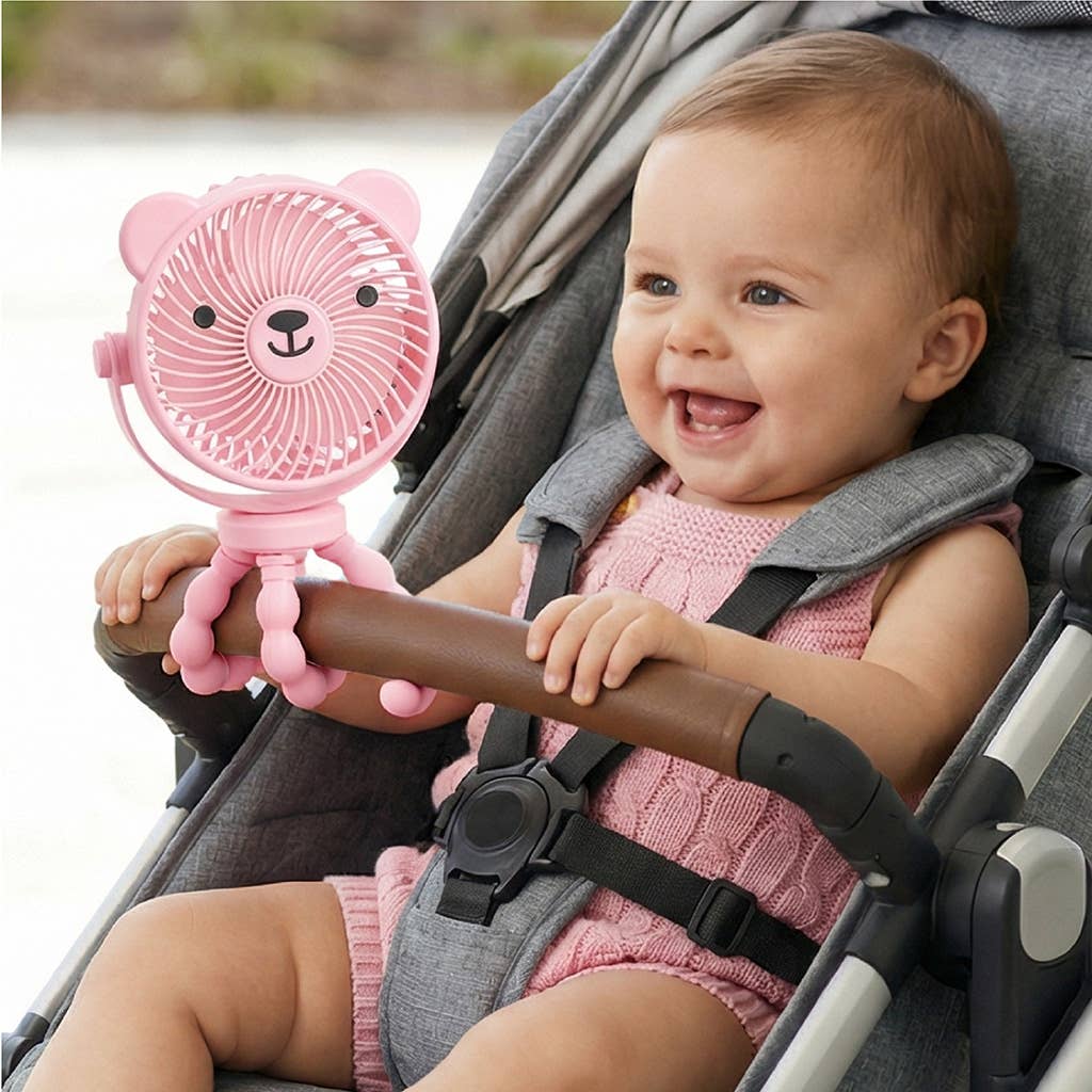 A baby sitting in a stroller holds a pink bear-shaped clip-on handheld fan attached to the stroller armrest.