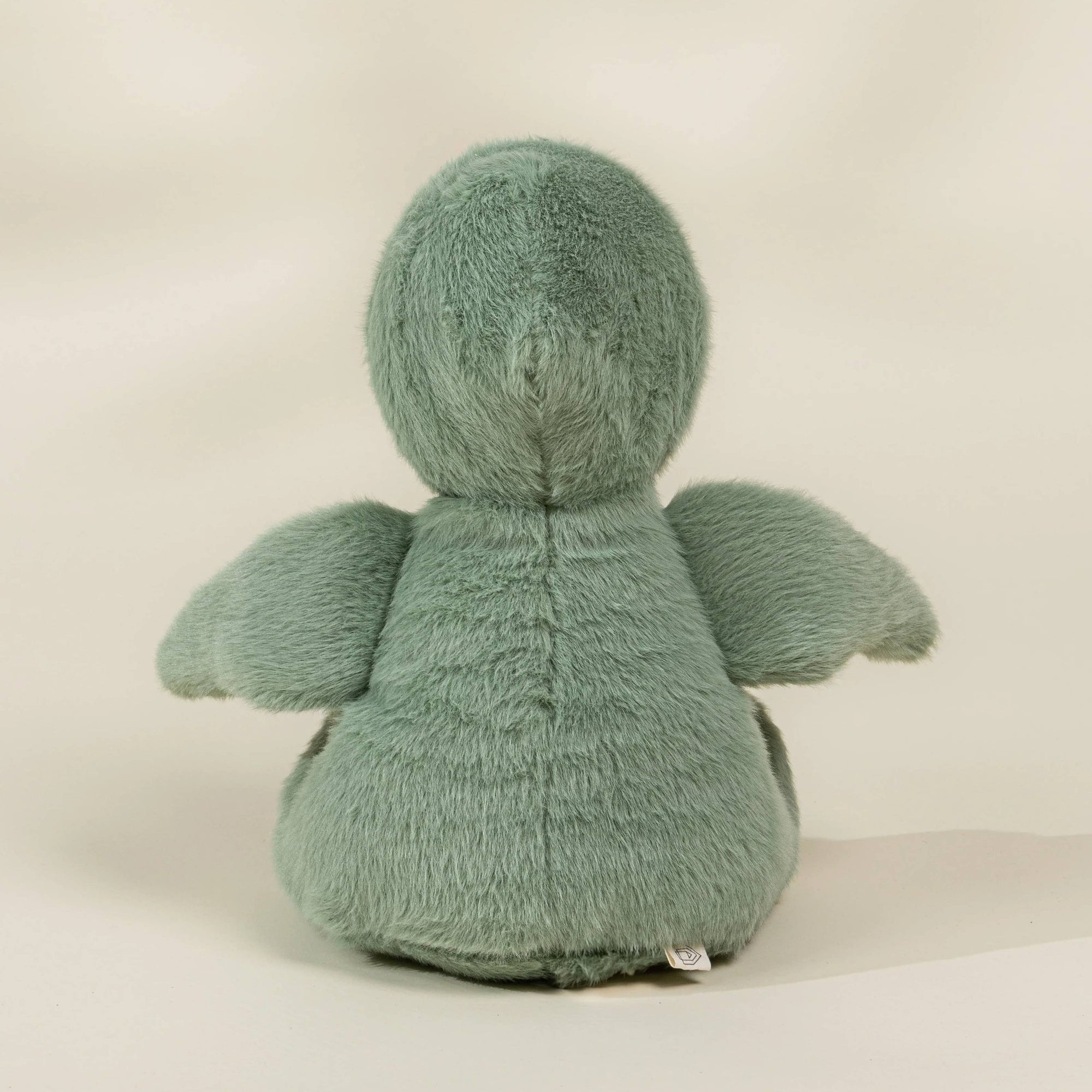 Green plush toy with wings on a beige background