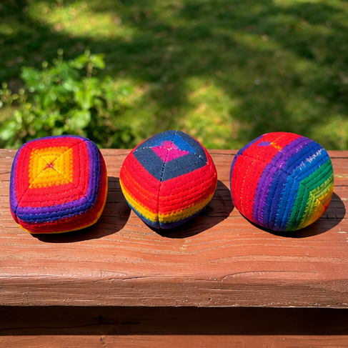 Three colorful hacky sacks on a wooden surface with a green outdoor background