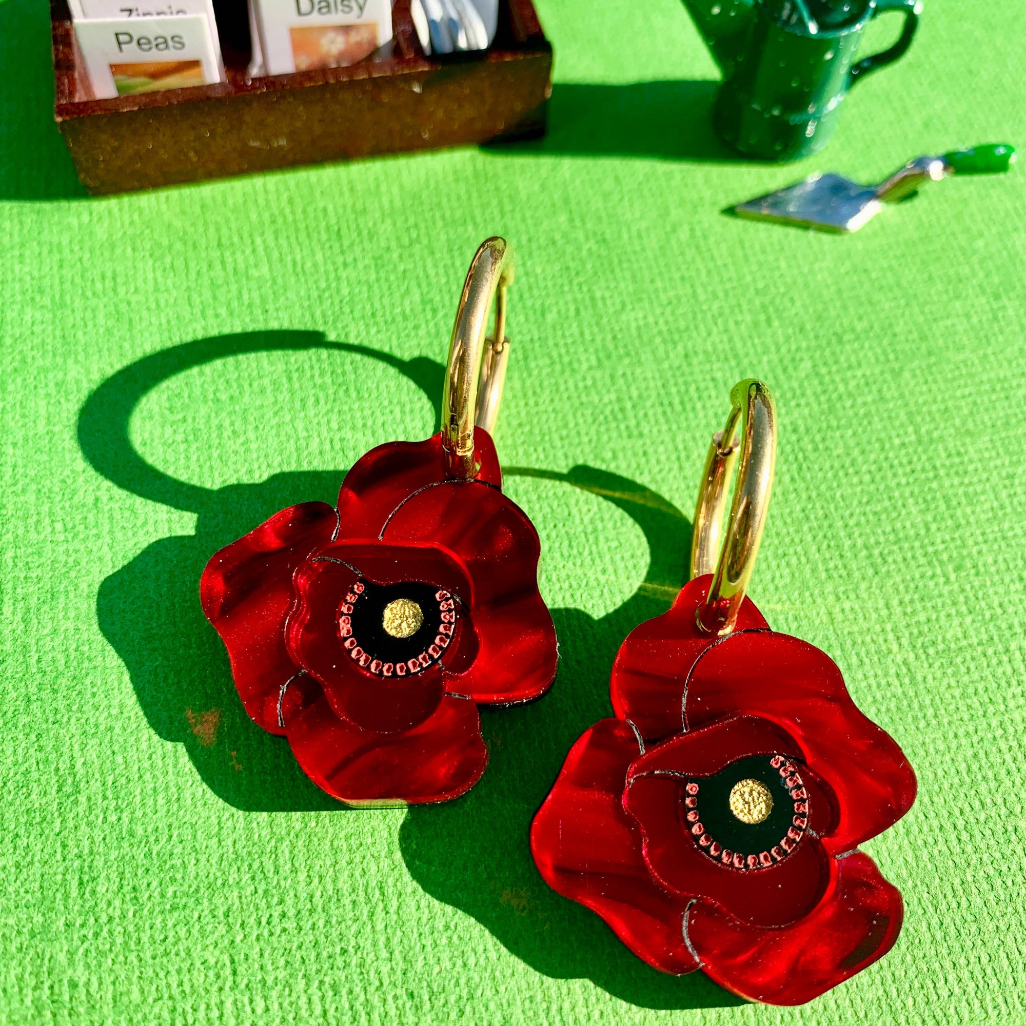 Red flower-shaped earrings on a green background with gardening-themed items.