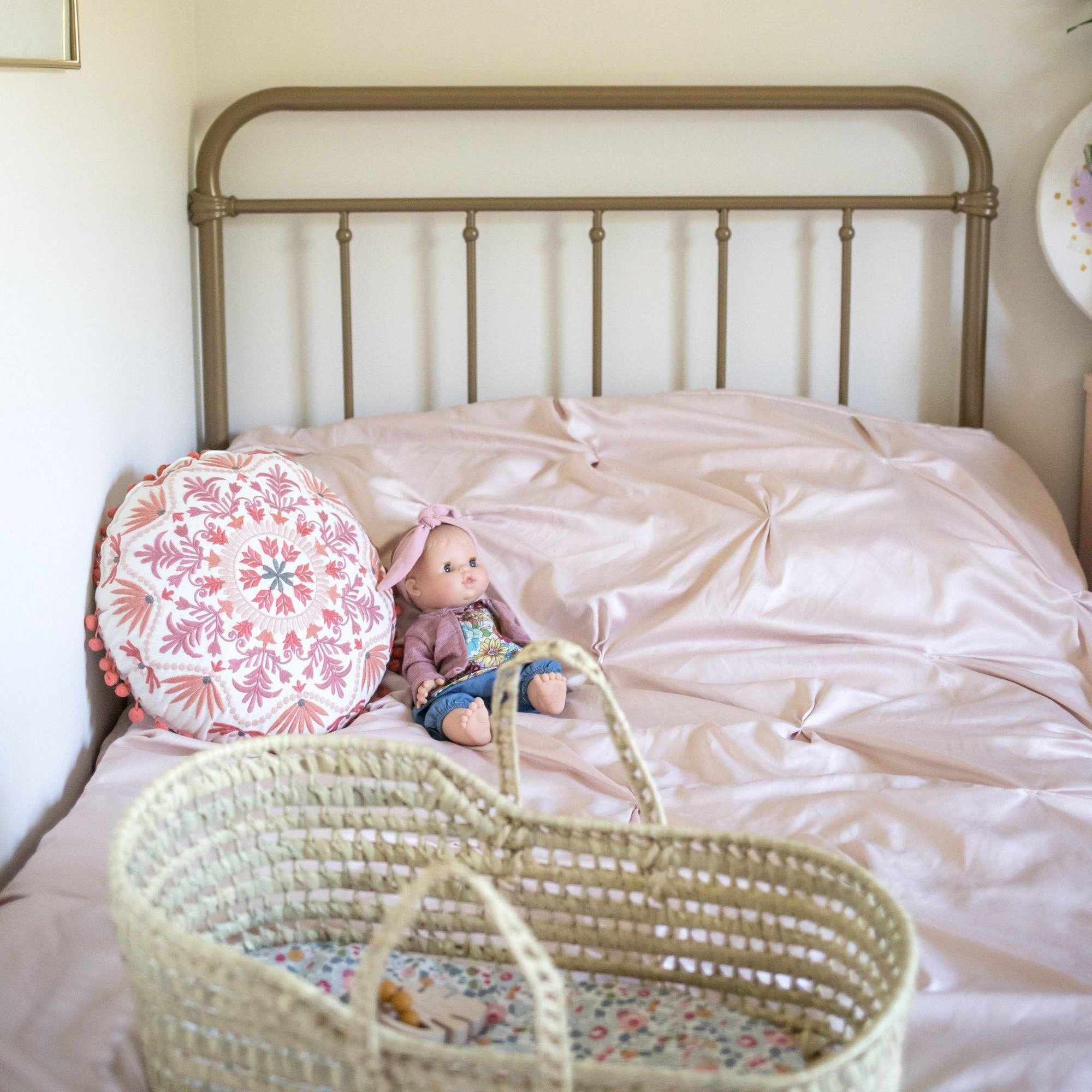Baby doll lying on a bed next to a wicker basket with a floral pattern