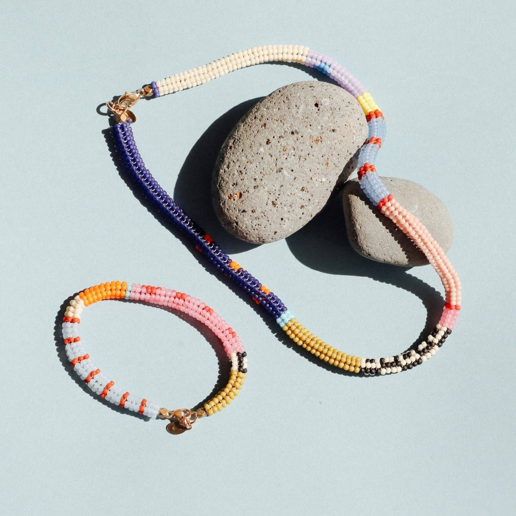Colorful beaded necklace and bracelet on a light blue background with stones.