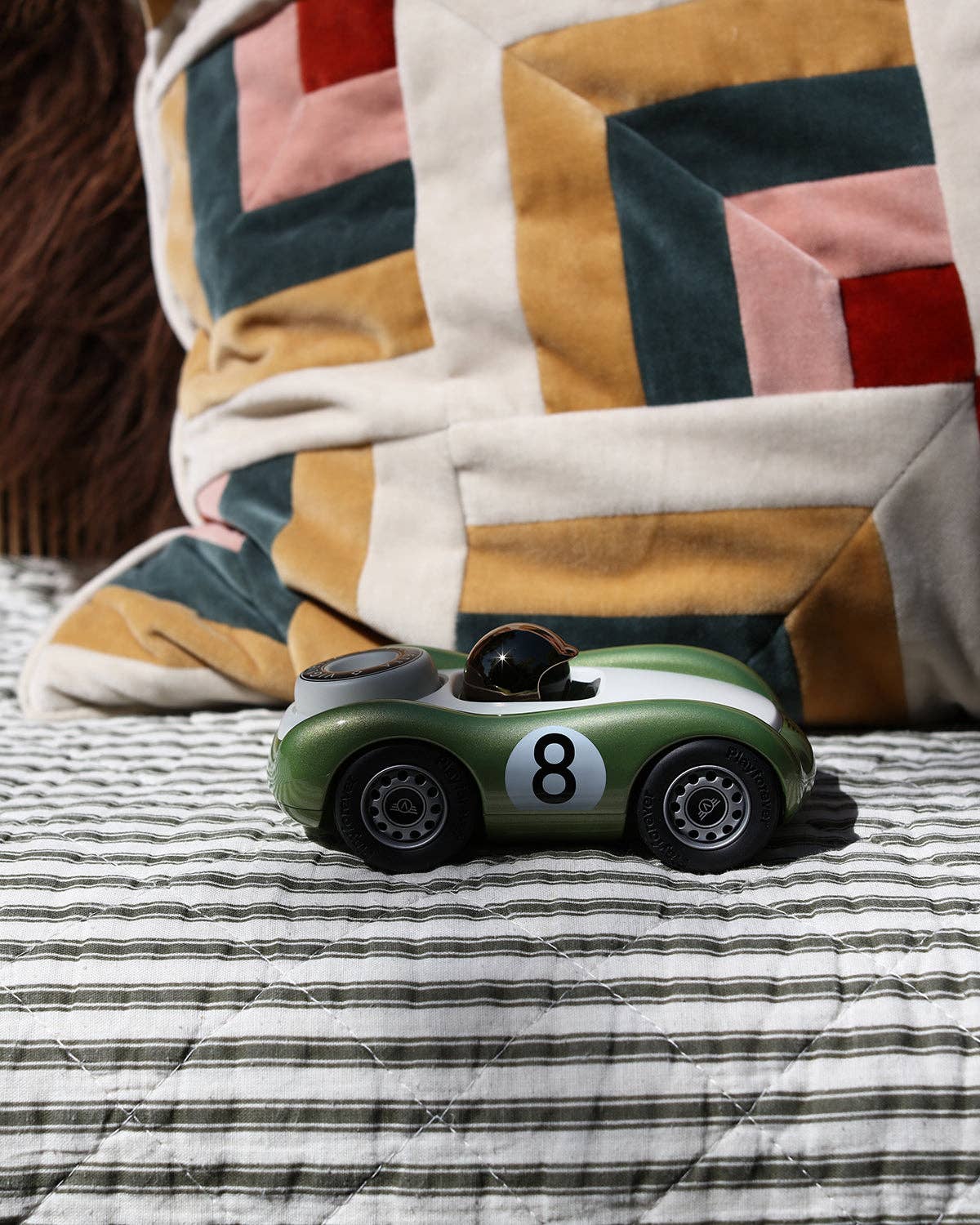 Toy car with the number 8 on a striped surface with a quilted blanket in the background