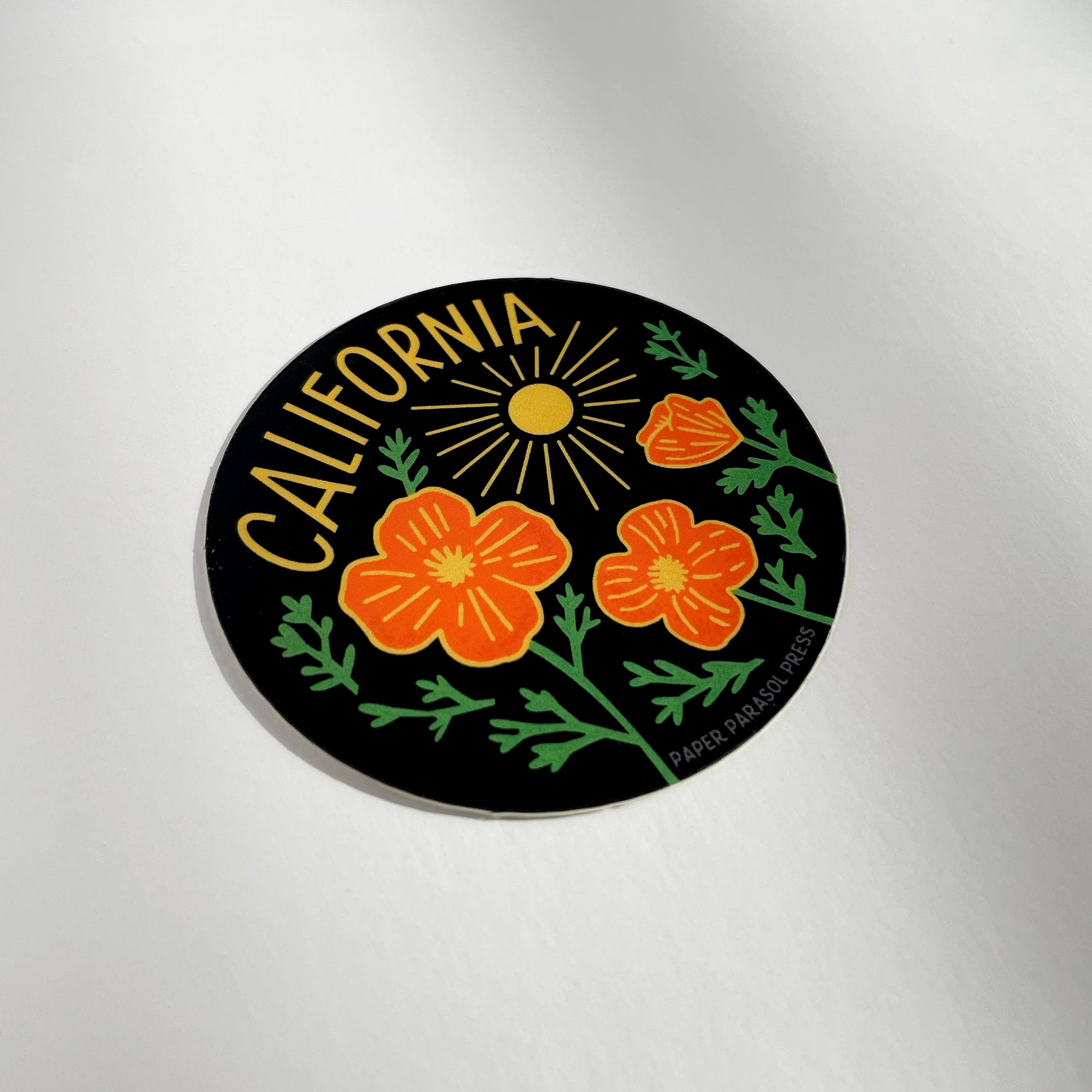 Round sticker with California text, sun, and flowers on a reflective surface