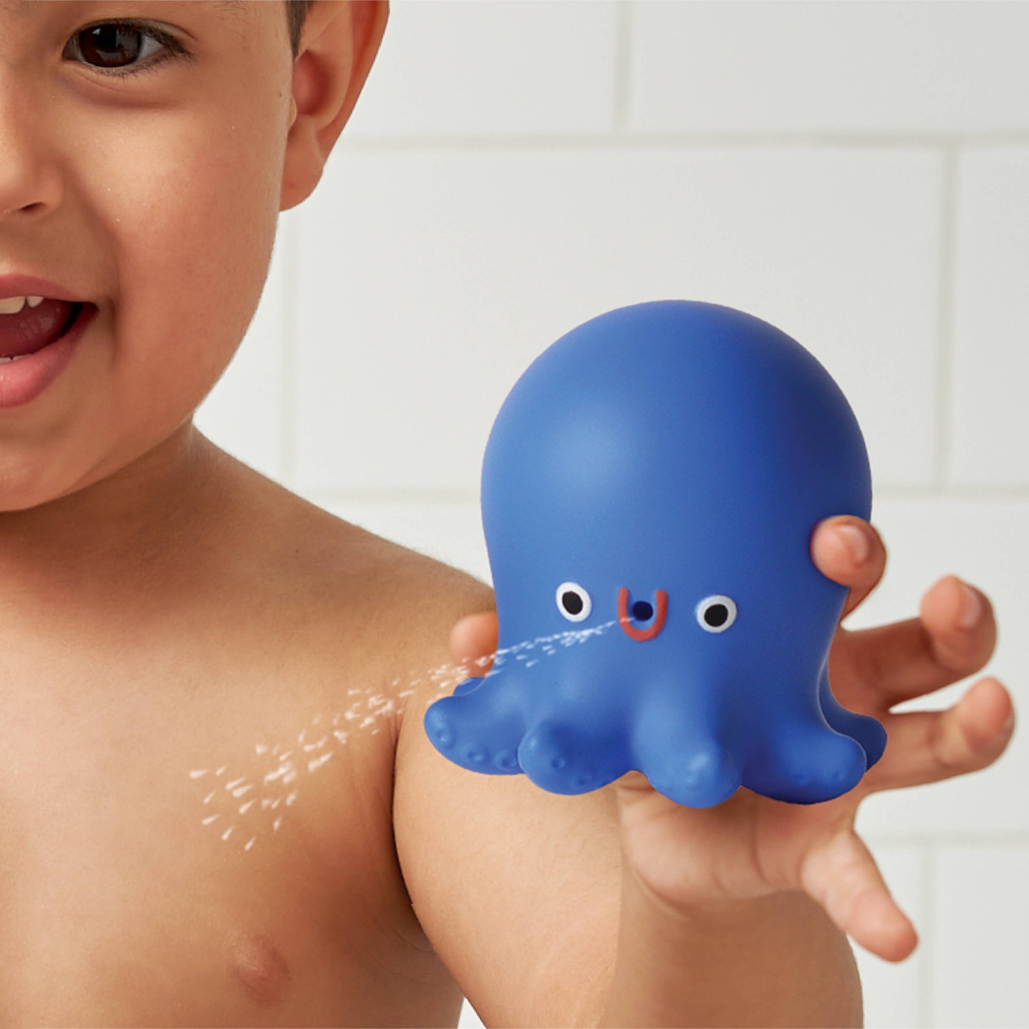 Child holding a blue octopus-shaped toy with water features in a bathroom setting