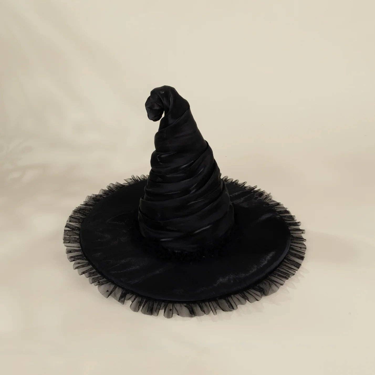 A black witch hat with a wide, frayed brim, photographed against a plain off-white fabric background.